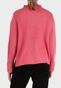 Maglione rosa a coste con collo alto, spalle scese e polsini ripiegati. Caratterizzato da una vestibilità rilassata e spacchi ai lati dell'orlo.