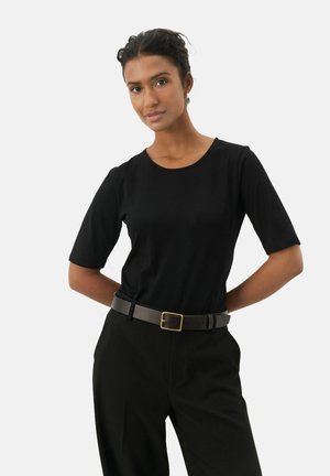Chemise noire à manches courtes en tissu doux avec un col rond, associée à un pantalon noir taille haute et une ceinture marron avec une boucle dorée.