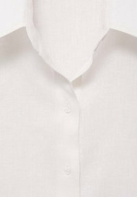 Camisa de lino blanca con cuello puntiagudo, que presenta una fila de botones y una tela texturada. Material suave y ligero con un brillo mínimo.