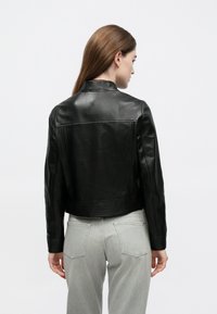 Μαύρο biker jacket από δέρμα με εφαρμοστή σχεδίαση, ραβδώσεις στη μέση και κλασικό γιακά, συνδυασμένο με ανοιχτό γκρι τζιν.