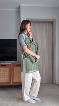 Grön oversizad jacka på en galge, knäppningsdesign, bärs med en ljusgrå t-shirt och creamfärgade vida byxor, i en modern interiör.