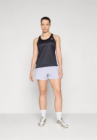Camiseta sin mangas deportiva negra y pantalones cortos gris claro. La tela es suave, con un logo en la camiseta sin mangas. Los pantalones cortos tienen un ajuste atlético.