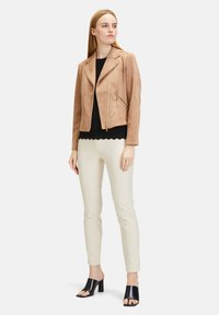 Tan suede motorcycle jacket with asymmetrical zipper, paired with a black top, ivory slim pants, and black open-toe mules.