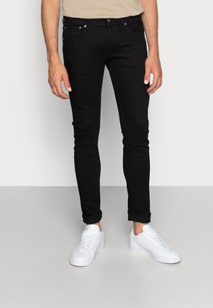 Jean slim noir en denim, doté de cinq poches, d'une fermeture à bouton et à zip, avec des ourlets retroussés, associé à des baskets blanches.