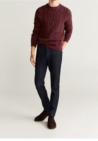 Pull en maille torsadée bordeaux avec col et ourlet côtelés, associé à un jean en denim foncé et des bottines marron.
