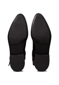 Chaussures noires avec semelles en caoutchouc, présentant une texture lisse et un design minimaliste. Le nom de la marque "Calvin Klein" est embossé sur les semelles.