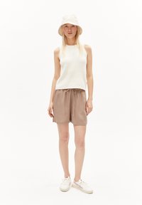 White ribbed tank top, beige drawstring shorts, and white sneakers with colored accents. Model wearing a light-colored bucket hat.