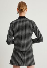 Sort-hvid ternet blazer med krave, fremstillet i et struktureret stof og lange ærmer, parret med en matchende mininederdel.