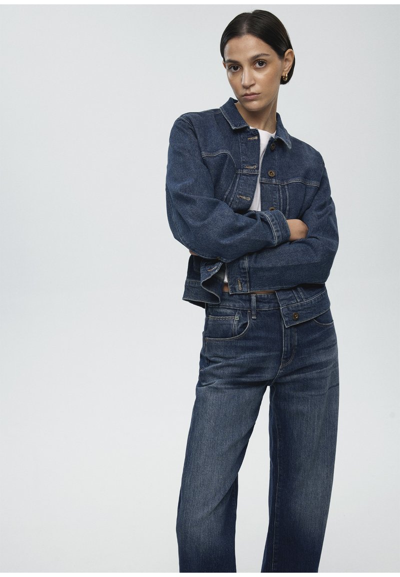 Denim jacket and jeans in dark wash. Jacket features button closure, chest pockets, and a cropped fit. Jeans with straight legs and standard pockets.