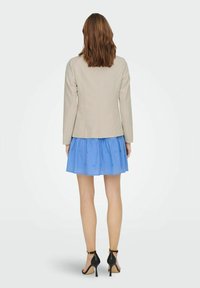 Beige skräddarsydd kavaj med långa ärmar som kombineras med en kort, ljusblå kjol med draperat tyg och subtila detaljer. Svarta sandaletter med remmar.
