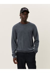 Dunkelgrauer Langarmpullover aus weichem Material, mit Rundhalsausschnitt und gerippten Bündchen, kombiniert mit dunklen Hosen.
