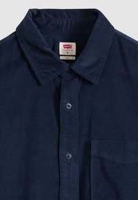 Σκούρο μπλε πουκάμισο κοτλέ με κουμπιά, γιακά και τσέπη στο στήθος, μέγεθος μεσαίο Levi's, ετικέτα με τη φράση "loose fit" ορατή μέσα στον γιακά.