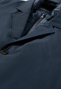 Giacca blu navy con una tessitura liscia, dotata di chiusura a bottoni, rever a punta e tasca interna con zip.