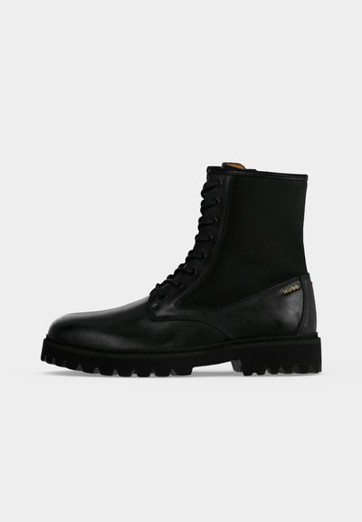 Botte à lacets en cuir noir et tissu avec semelle épaisse à crampons et petit logo doré sur le côté.