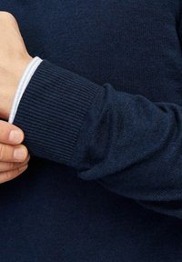 Granatowy sweter z dzianiny z prążkowanymi mankietami. Mankiet ma cienką białą prążkowaną podszewkę, co stanowi kontrast dla ciemnej tkaniny. Miękka faktura.