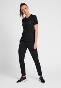 Svart atletisk t-shirt med korta ärmar och rundad halsringning, tillsammans med svarta joggers och svarta sneakers, skapar en enhetlig sportklädeslook.