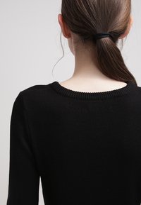 Czarny dziergany sweter z okrągłym dekoltem, prezentujący miękką teksturę i dopasowany krój, widziany od tyłu z włosami związanymi w kucyk.