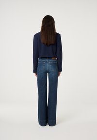 Sweater azul-marinho cortado com mangas longas, combinado com jeans de denim azul de cintura alta e perna larga, com bolsos traseiros e bainha crua.