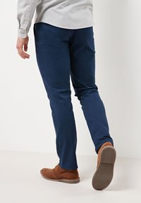 Marineblå chinos lavet af en bomuldsblanding, med en slim fit, glat tekstur og en flad frontdesign, parret med brune ruskindsko.