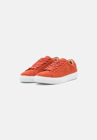 Red suede sneakers with white rubber soles. Features include round laces and minimalistic design, showcasing a smooth, textured finish.