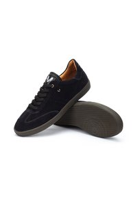 Zapatillas de ante negras con cierre de cordones, suela de goma marrón en contraste, acentos perforados y una etiqueta de logo en la lengüeta.
