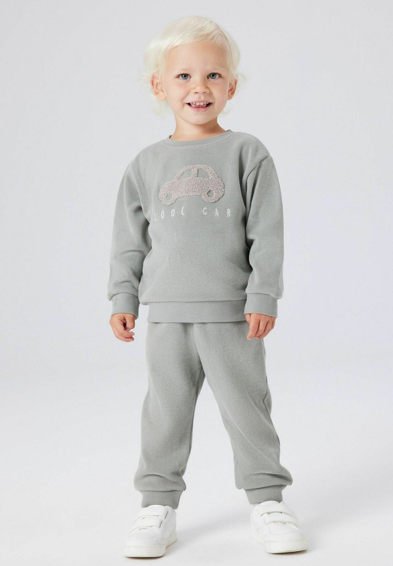 Szary dres bawełniany z fakturowanym nadrukiem samochodu i napisem "COOL CAR", zestawiony z białymi trampkami, na tle jednolitego tła.