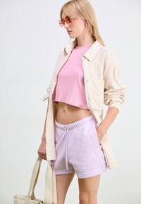 Light striped button-up shirt, pink cropped tank top, lavender shorts with logo, and canvas tote bag. Accessories include pink rectangular sunglasses.