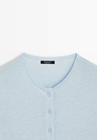 Světlomodrý kardigan na knoflíky s kulatým výstřihem a třemi knoflíky, uvnitř límce s černou štítkem s informacemi o značce.