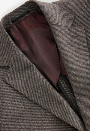 Blazer gris texturé avec un col cranté, présentant une doublure à motif bordeaux. Coutures visibles et poche intérieure sur le côté gauche.