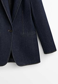 Blazer en denim bleu foncé avec fermeture à un bouton noir, revers crantés, deux poches avant passepoilées et détails de surpiqûres contrastantes.