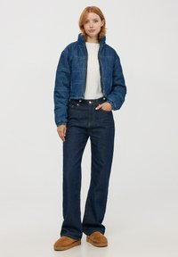 Kurtka bombka z denimu w ciemnoniebieskim kolorze z pikowanym wzorem i ściągaczami, zestawiona z jeansami z wysokim stanem w niebieskim kolorze oraz brązowymi butami na płaskiej podeszwie.