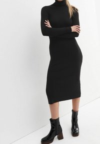 Svart ribbat polotröja klänning, långa ärmar, längd till mitten av vaden, gjort av sträckt tyg, tillsammans med svarta klackade anklar stövlar för kontrast.