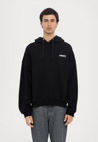 Schwarzer Kapuzenpullover mit kleinem weißem Logo auf der Brust, aus weichem Material, mit gerippten Bündchen und Saum.