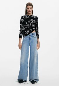 Svart långärmad topp med vita abstrakta mönster, tillsammans med ljusblå högmidjade vida jeans med en subtil fransad fåll.