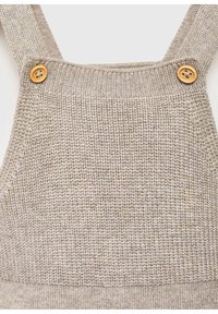 Top senza maniche in maglia beige con due bottoni di legno che fissano le spalline, caratterizzato da una texture a coste e un scollo quadrato.