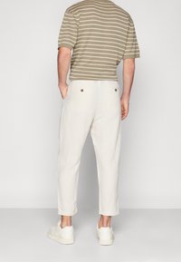 Vita linnebyxor med avslappnad passform och kortade ben, med bakfickor som har guldfärgade knappdetaljer. Bärs med en randig beige topp.