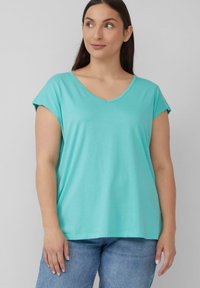 Een turquoise T-shirt met korte mouwen en V-hals, gemaakt van zachte stof, met een relaxte pasvorm en een gladde textuur, gecombineerd met lichtblauwe spijkerbroek.