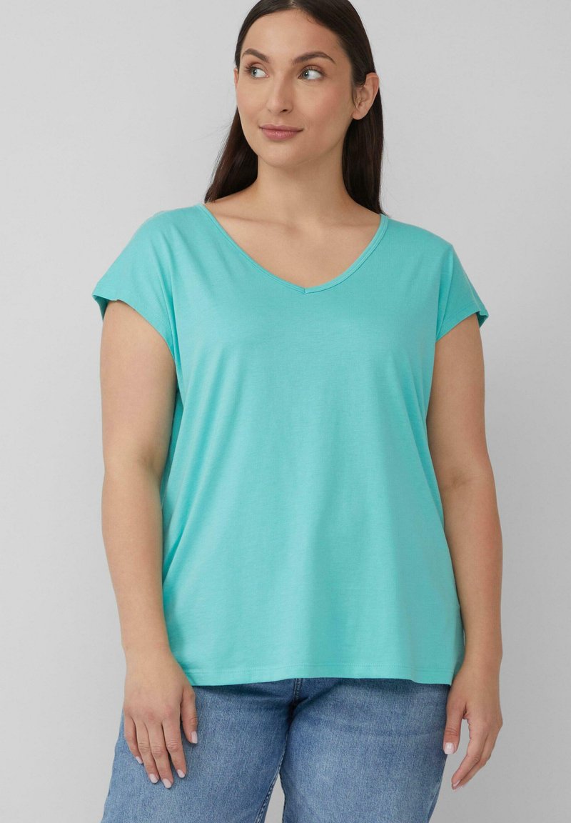 Een turquoise T-shirt met korte mouwen en V-hals, gemaakt van zachte stof, met een relaxte pasvorm en een gladde textuur, gecombineerd met lichtblauwe spijkerbroek.
