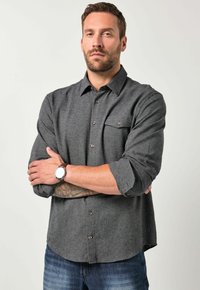 Grå skjorte med lange ærmer, to brystlommer og brune knapper. Bæret med denimjeans. Glat tekstur og afslappet pasform.