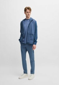 Blue hooded jacket with drawstrings, matching blue t-shirt, and slim-fit pants. Features a textured sleeve and white sneakers.