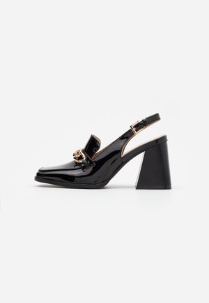Zapatos de tacón con tira trasera de charol negro, punta puntiaguda y tacón grueso. Cuentan con un adorno decorativo de metal en tono dorado.