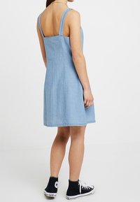 Ljusblå denimklänning med fyrkantig rygg, tunna axelband och en utsvängd kjol. Matchad med svarta högskaftade sneakers. Slät textur.