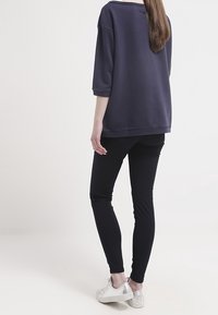 Felpa oversize navy con maniche a tre quarti, abbinata a jeans skinny neri e sneakers argento metallizzato. Design semplice, senza motivi.