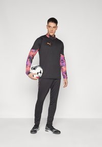 Fekete sportfelső színes mintás ujjal, hozzá illő fekete nadrággal és fekete-fehér focilabdával. A mellkason Puma logó található.