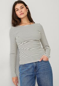 Langärmliges gestreiftes Oberteil in Creme und Marineblau, aus geripptem Material mit einem Boots-Ausschnitt. Kombiniert mit blauen Jeans.
