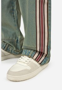 Tenisice s kremasto bijelim gornjim dijelom i akcentima od sive antilop kože, uparene s svijetloplavim trapericama koje imaju višebojnu prugastu bočnu ploču.