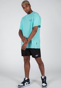 Camiseta turquesa de manga corta, pantalones cortos negros y zapatillas altas multicolores. Logo notable en la camiseta y los pantalones cortos. Textura suave.