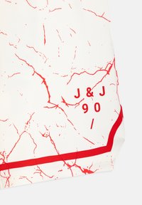 Tissu blanc avec des veines rouge marbrées et le texte rouge "J & J 90 /" au-dessus d'une bande rouge horizontale près du bord.