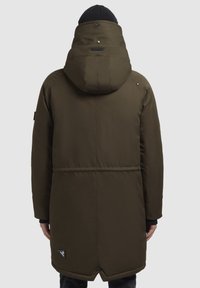 Kaki parka med huva, som har en mjuk textur, tryckknappar, sidofickor och en logotypapplikation nära fållen. Designen är midilång.
