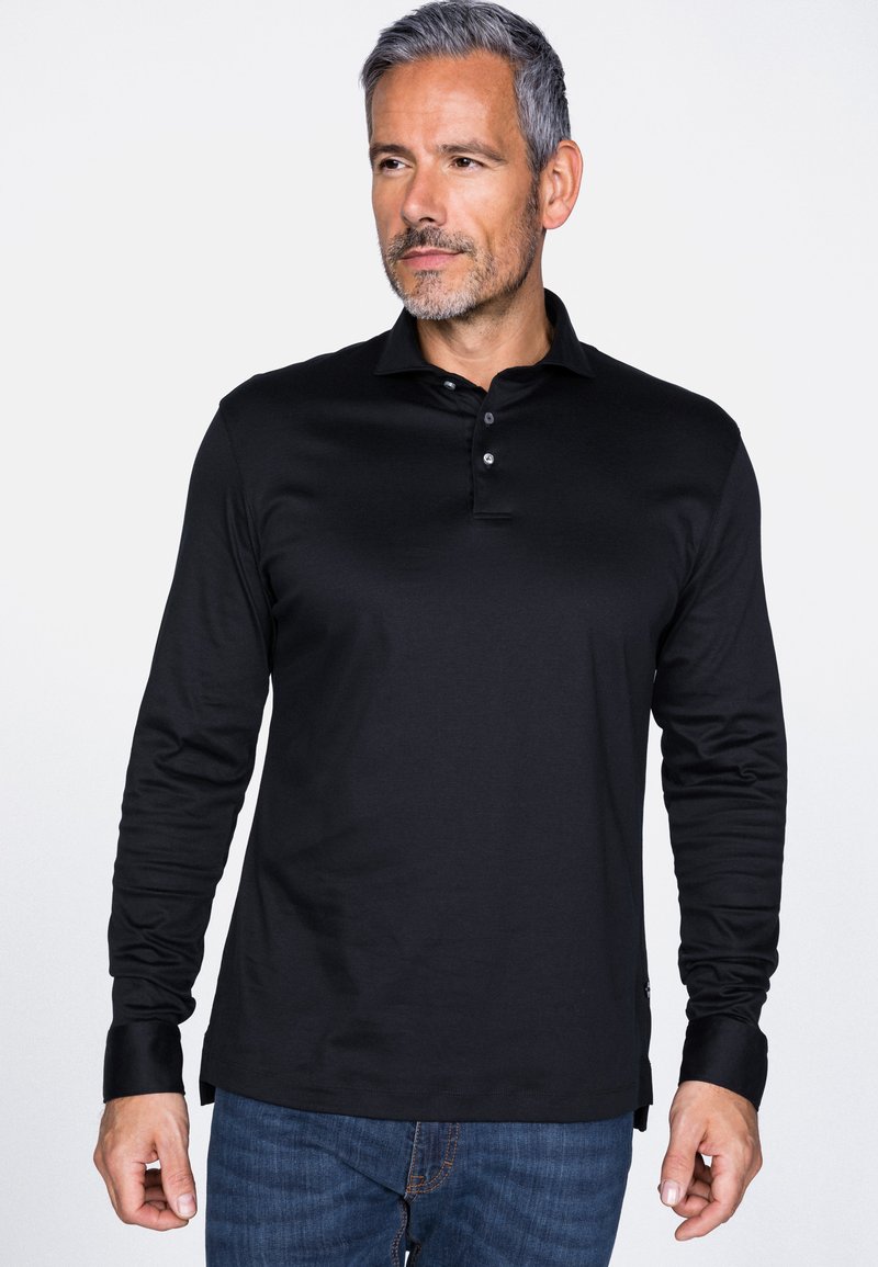 Schwarz langärmliges Polo-Shirt mit einer Knopfleiste mit drei Knöpfen, weichem Material und farblich abgesetzten Manschetten, kombiniert mit blauen Jeans.